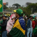 Father and child wrapped in Brazil flag at an outdoor gathering advocating democracy.