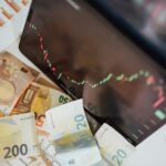 Close-up of euro banknotes with a digital stock market chart displaying a downward trend, symbolizing financial volatility.