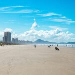 Enjoy a sunny day at Praia Grande's urban beach in São Paulo, Brazil, with scenic mountains and vibrant cityscape.