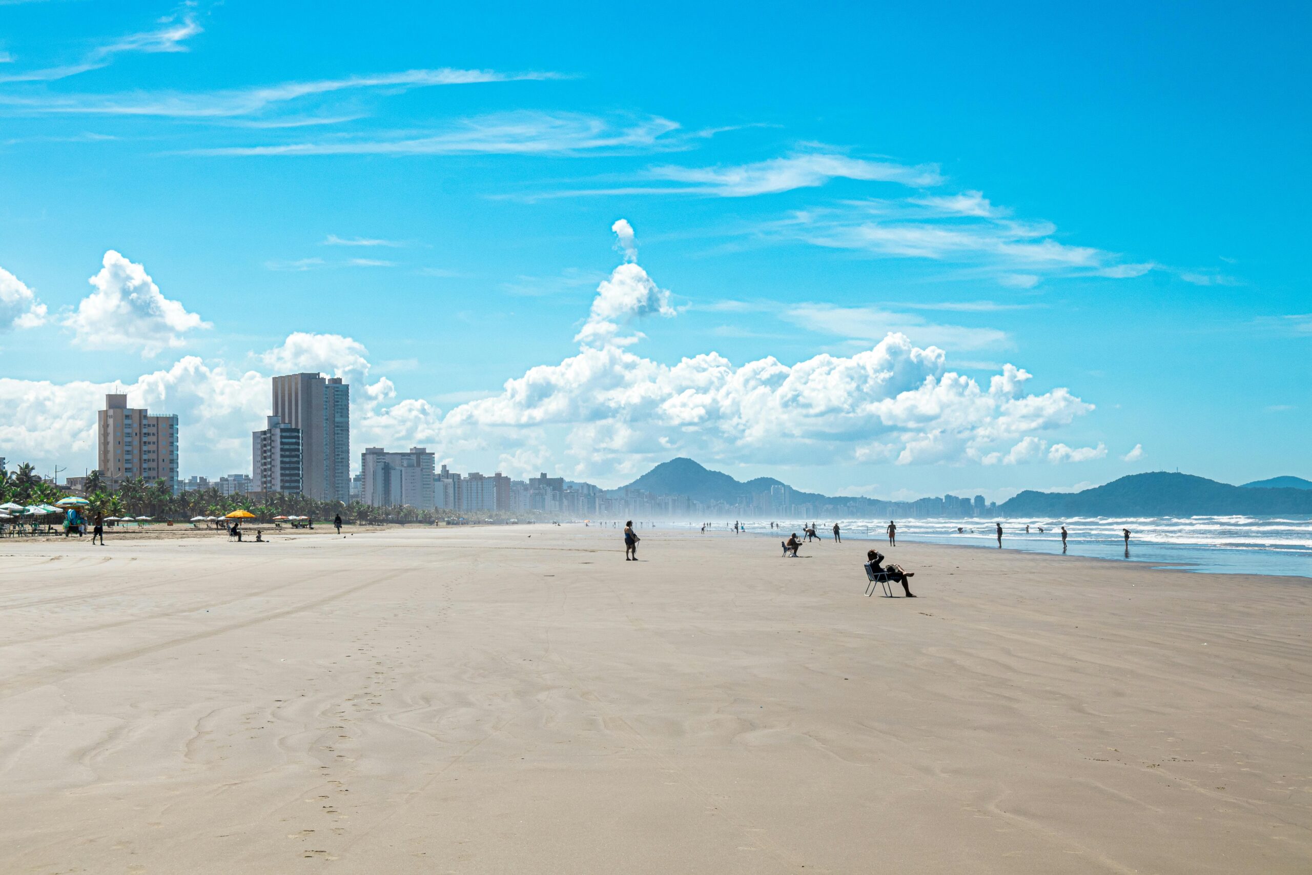 Enjoy a sunny day at Praia Grande's urban beach in São Paulo, Brazil, with scenic mountains and vibrant cityscape.