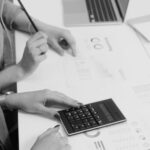 Two colleagues reviewing financial reports with a calculator in a modern workspace.