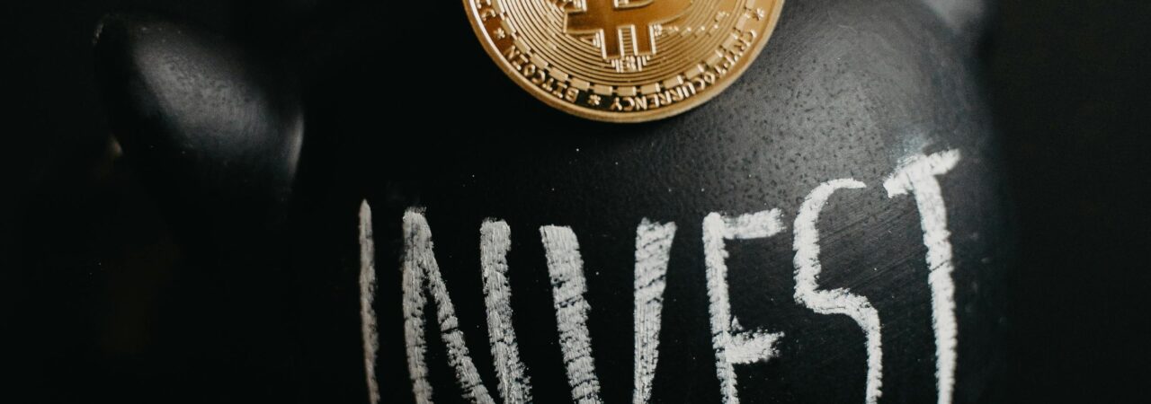 Gold bitcoin inserted into a black piggy bank labeled 'Invest', symbolizing cryptocurrency saving.